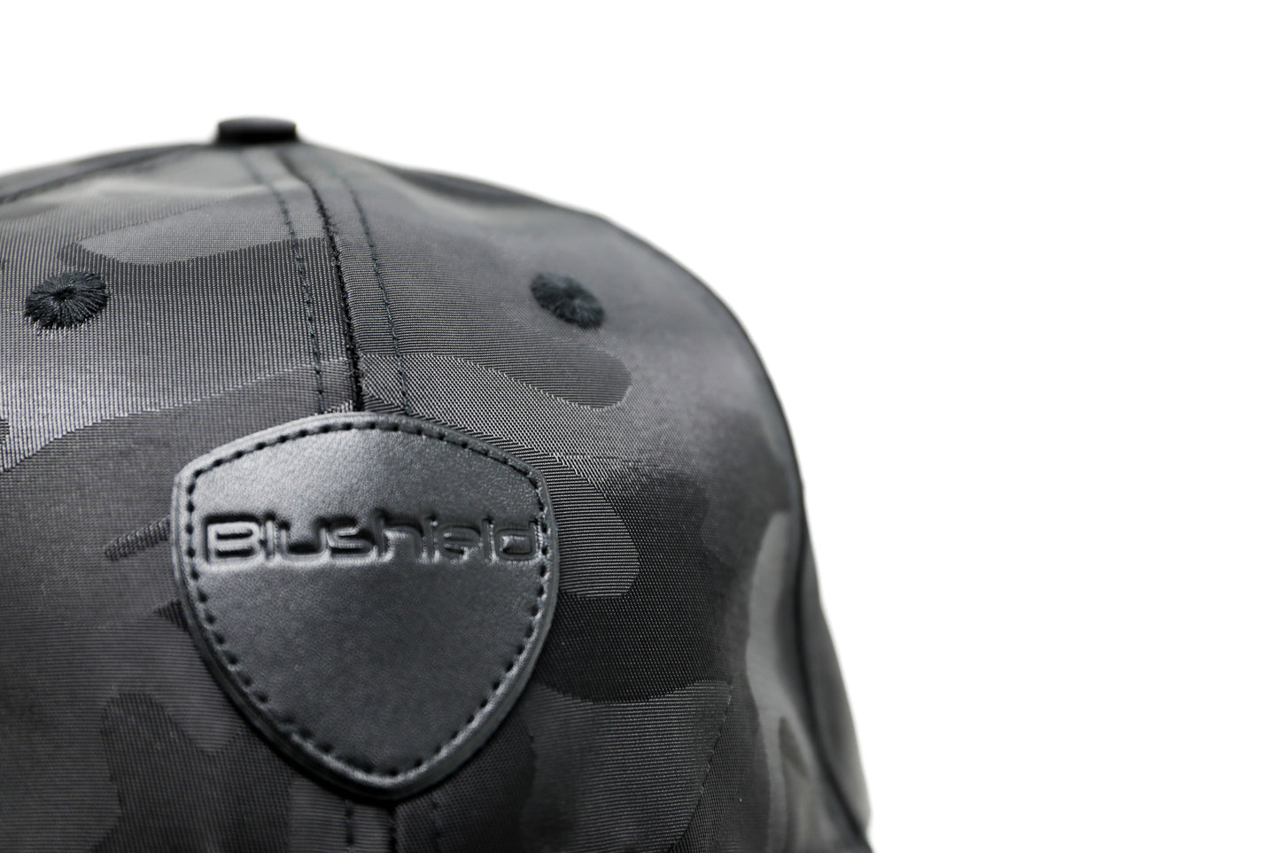 
                  
                    EMF PROTECTION  - Photo of Blushield black camo low radiation cap, closeup front view of logo
                  
                