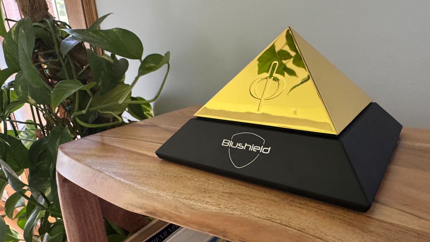 
                  
                    Pyramid-shaped device with gold top and black base on a wooden surface
                  
                